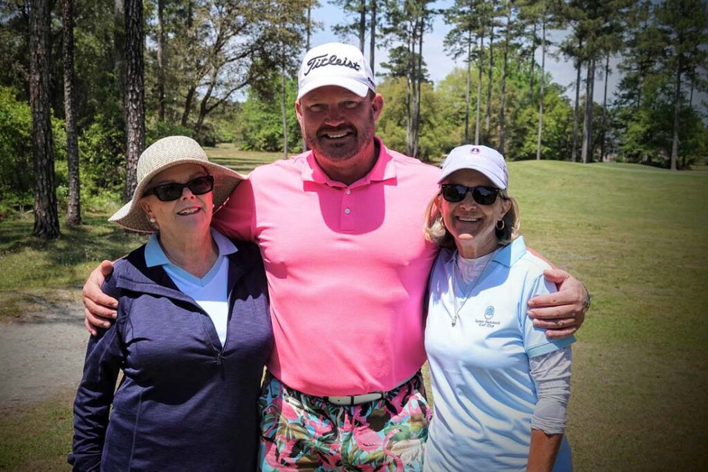 Three people smiling on a golf course.