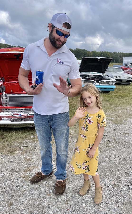 Man and girl waving at car show.