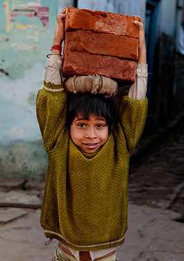 Child carrying bricks on their head.