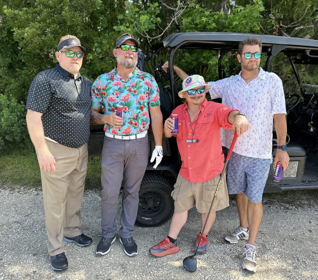 Four men posing by a golf cart.