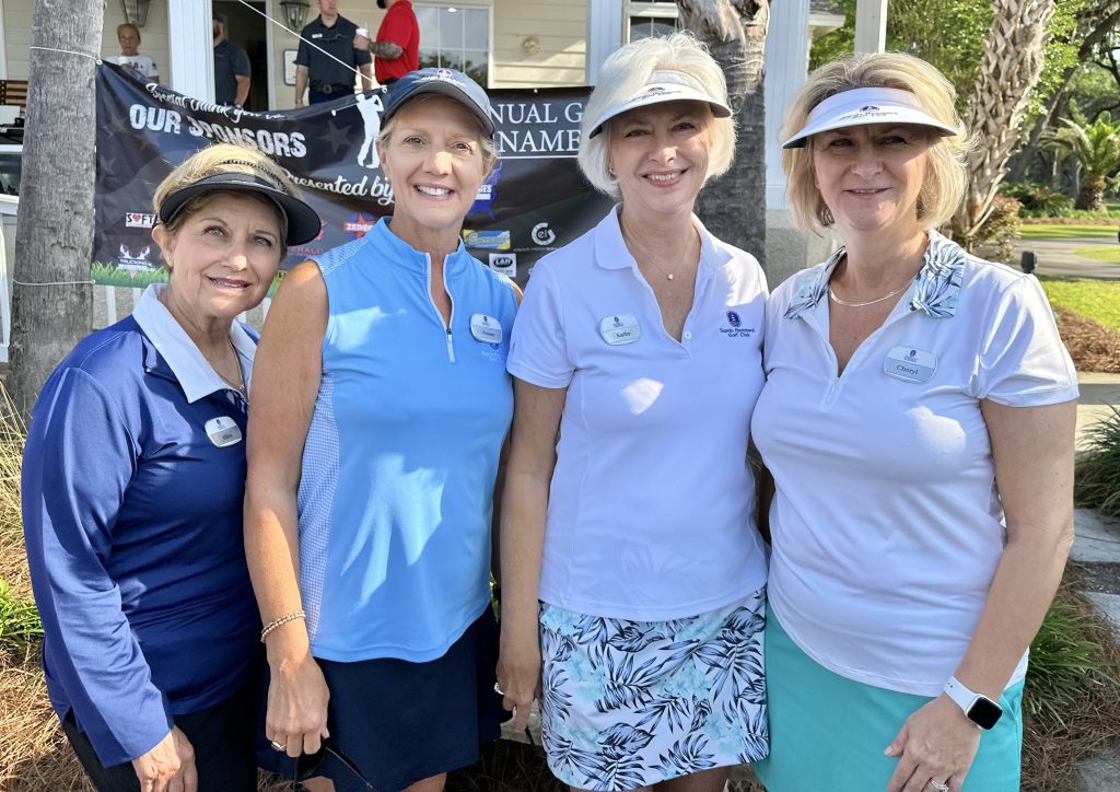 Four women in golf attire smiling outdoors.